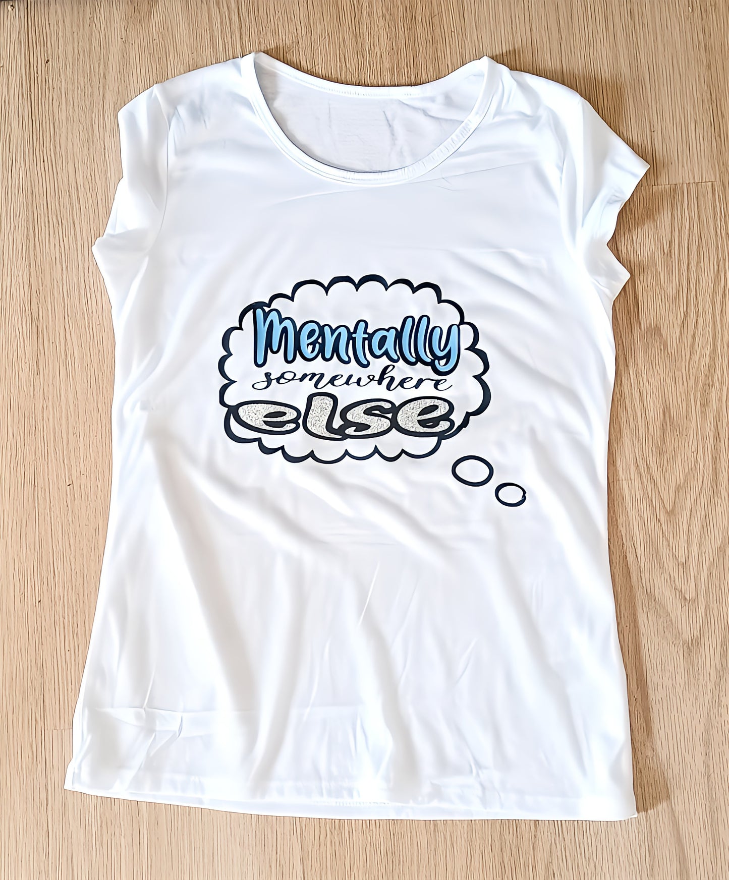 White t-shirt with 'Mentally somewhere else' text design on wooden floor