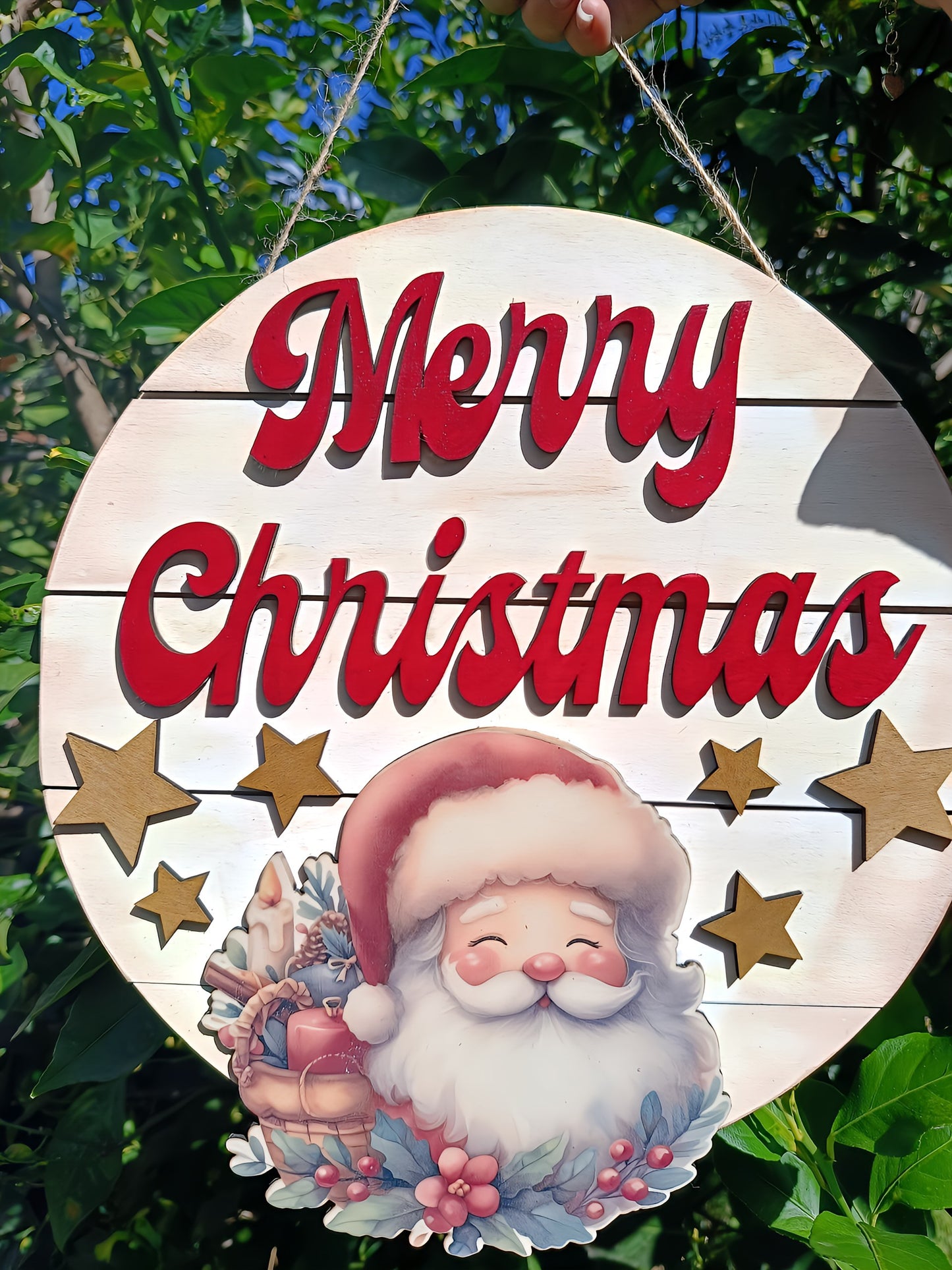 Merry Christmas sign with cute Santa and stars, hanging outdoors among green leaves