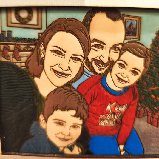 Ornamento natalizio in legno inciso con famiglia cartoon davanti all’albero di Natale e scritta “Buon Natale!”