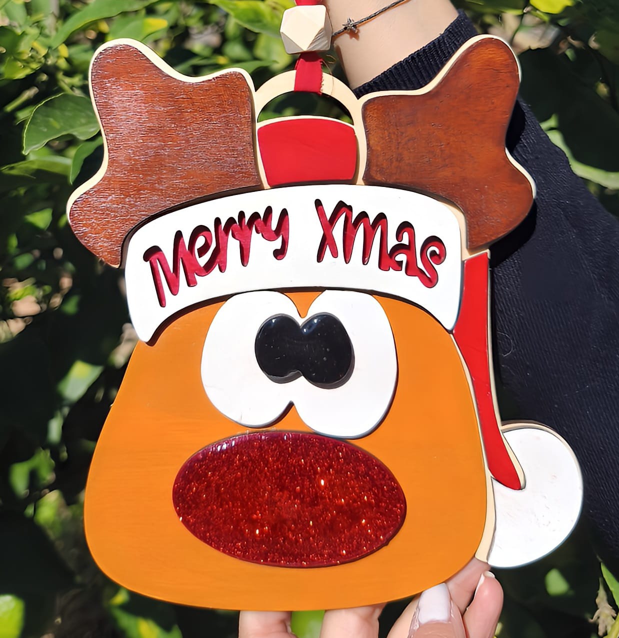 Hand holding a reindeer Christmas ornament with Merry Xmas text and glitter red nose