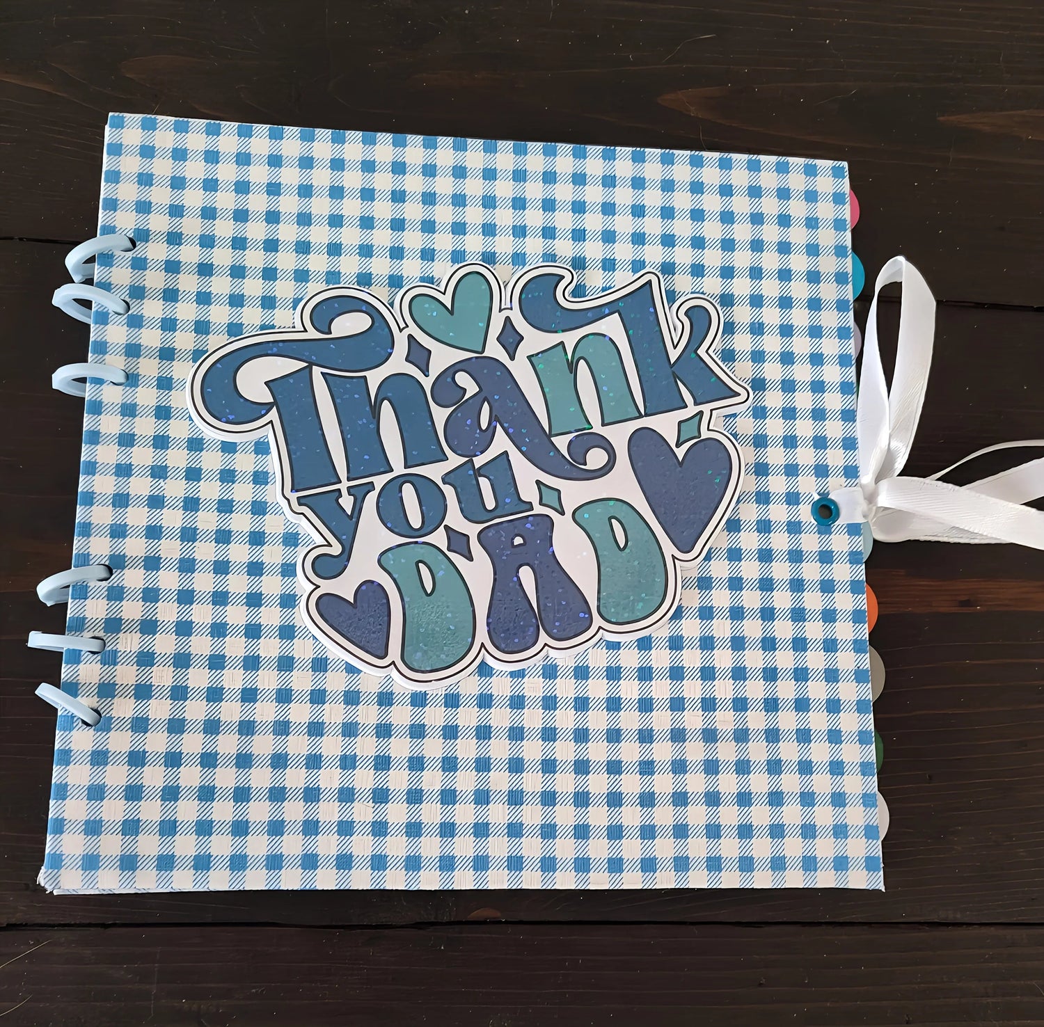 Blue checkered scrapbook with 'Thank you Dad' and hearts on the cover, ribbon tied, gift idea