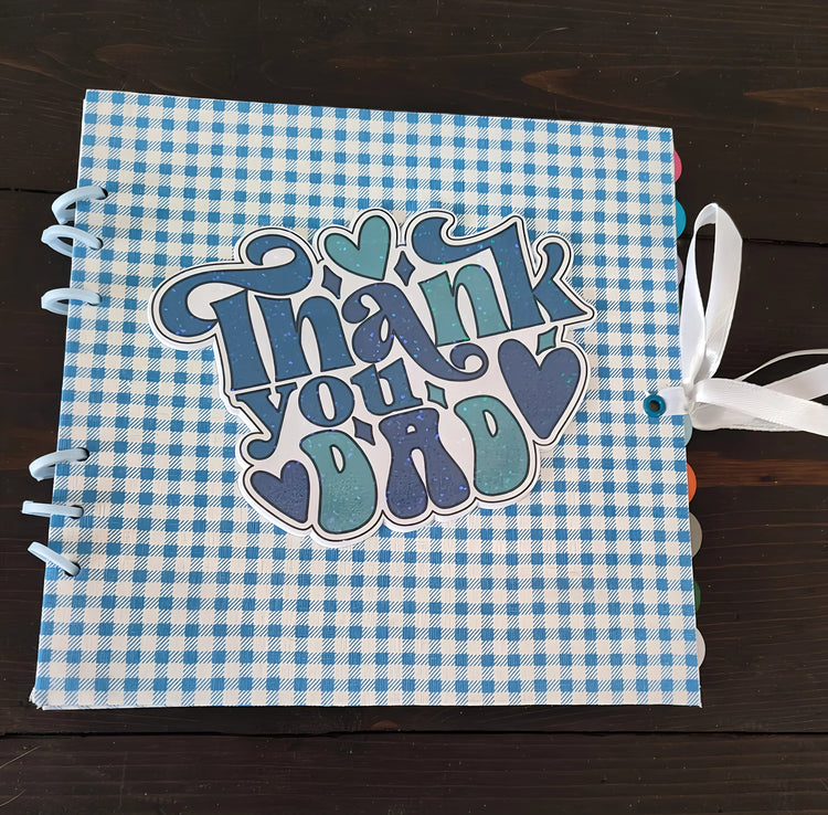 Blue checkered scrapbook with 'Thank you Dad' and hearts on the cover, ribbon tied, gift idea
