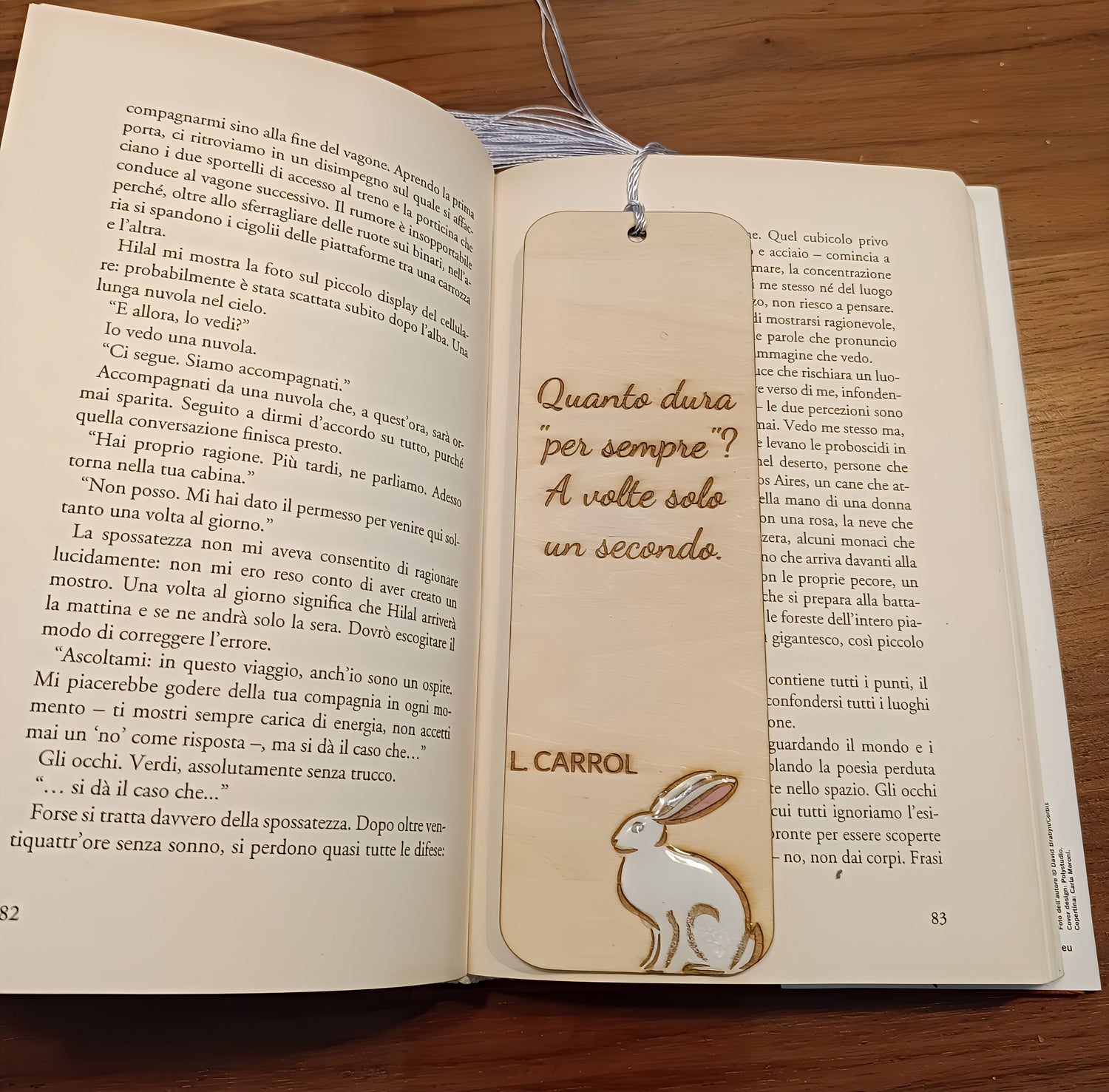 Open book on wooden table with engraved wooden rabbit bookmark and Italian quote by L. Carrol