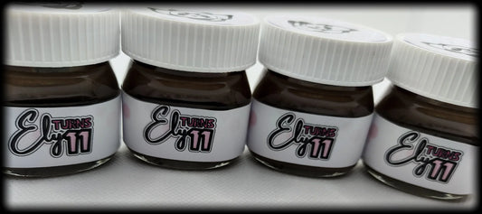 Small chocolate jars with white lids labeled 'Ely turns 11' for birthday party favors