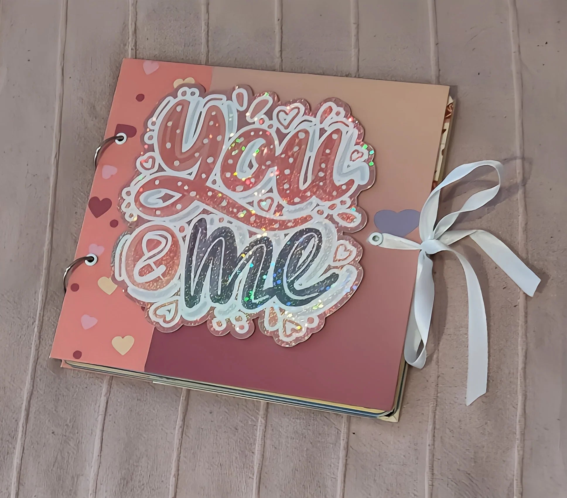 Handmade scrapbook album with 'You & me' glitter cover, heart designs, and ribbon bow