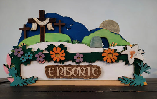 Wooden Easter resurrection scene with three crosses, flowers, and sign reading 'È risorto'.