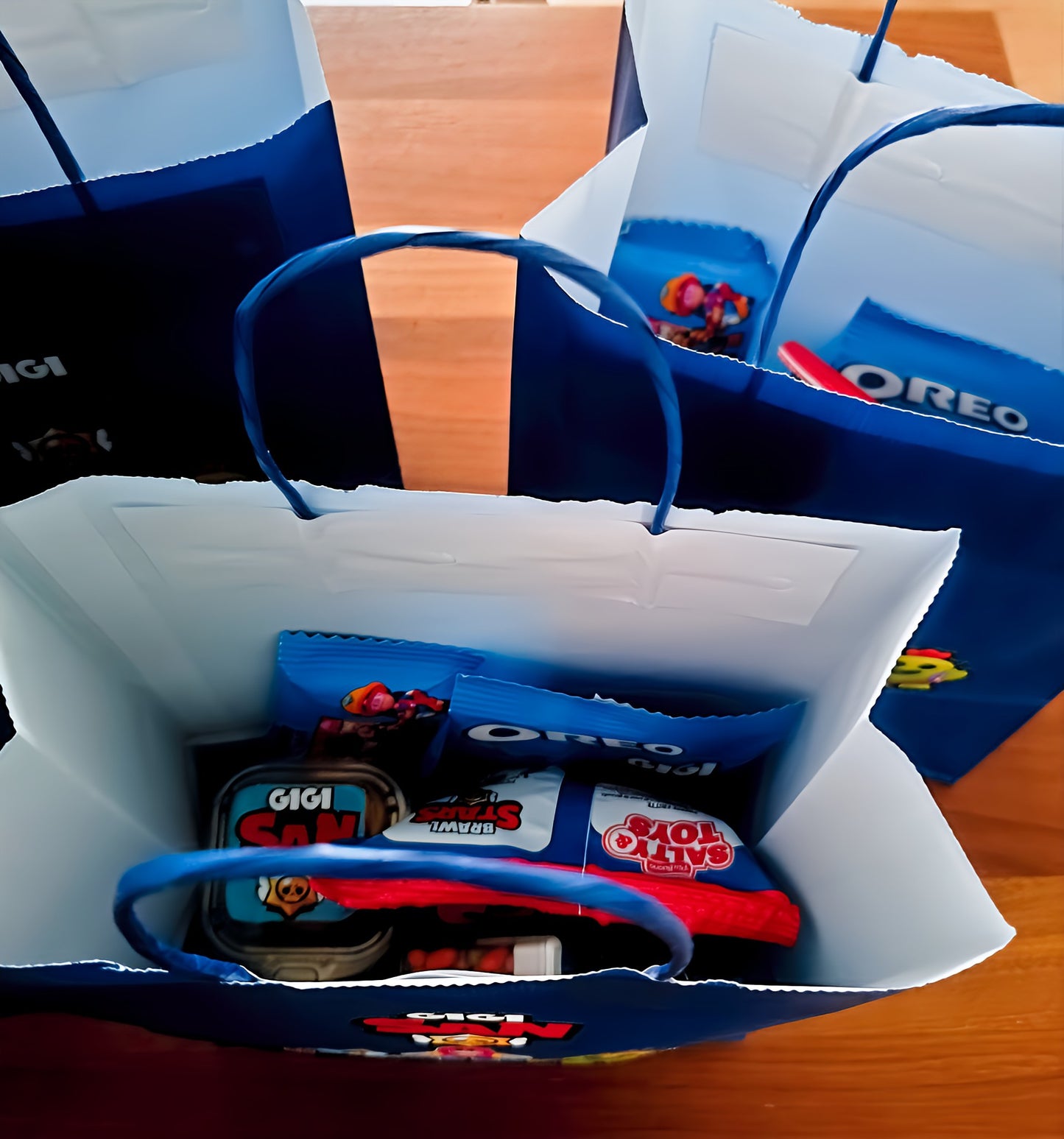 Blue gift bags with Oreo packets, Gigi snacks, treats, on a wooden table