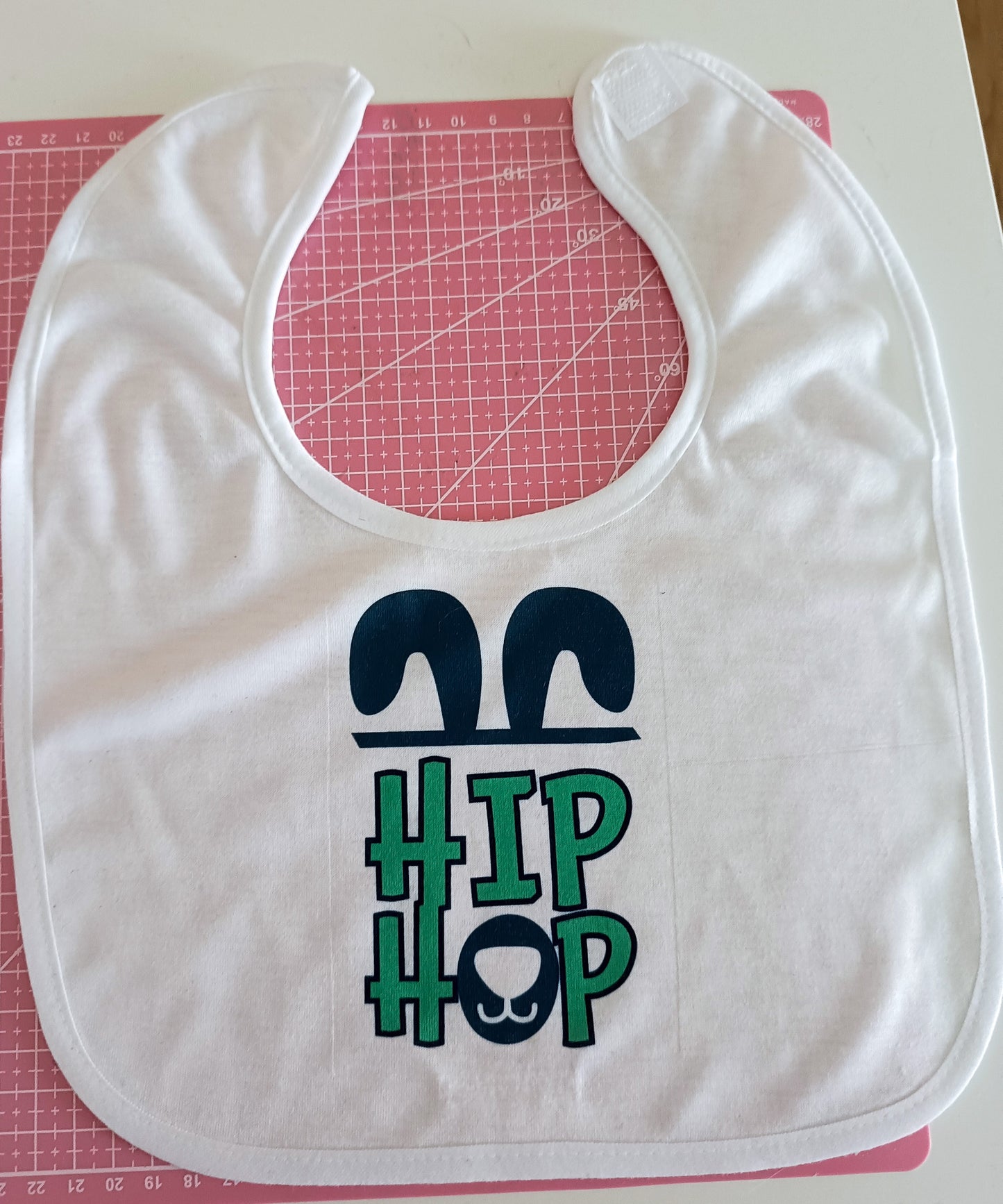 White baby bib with 'HIP HOP' bunny ears design on pink cutting mat