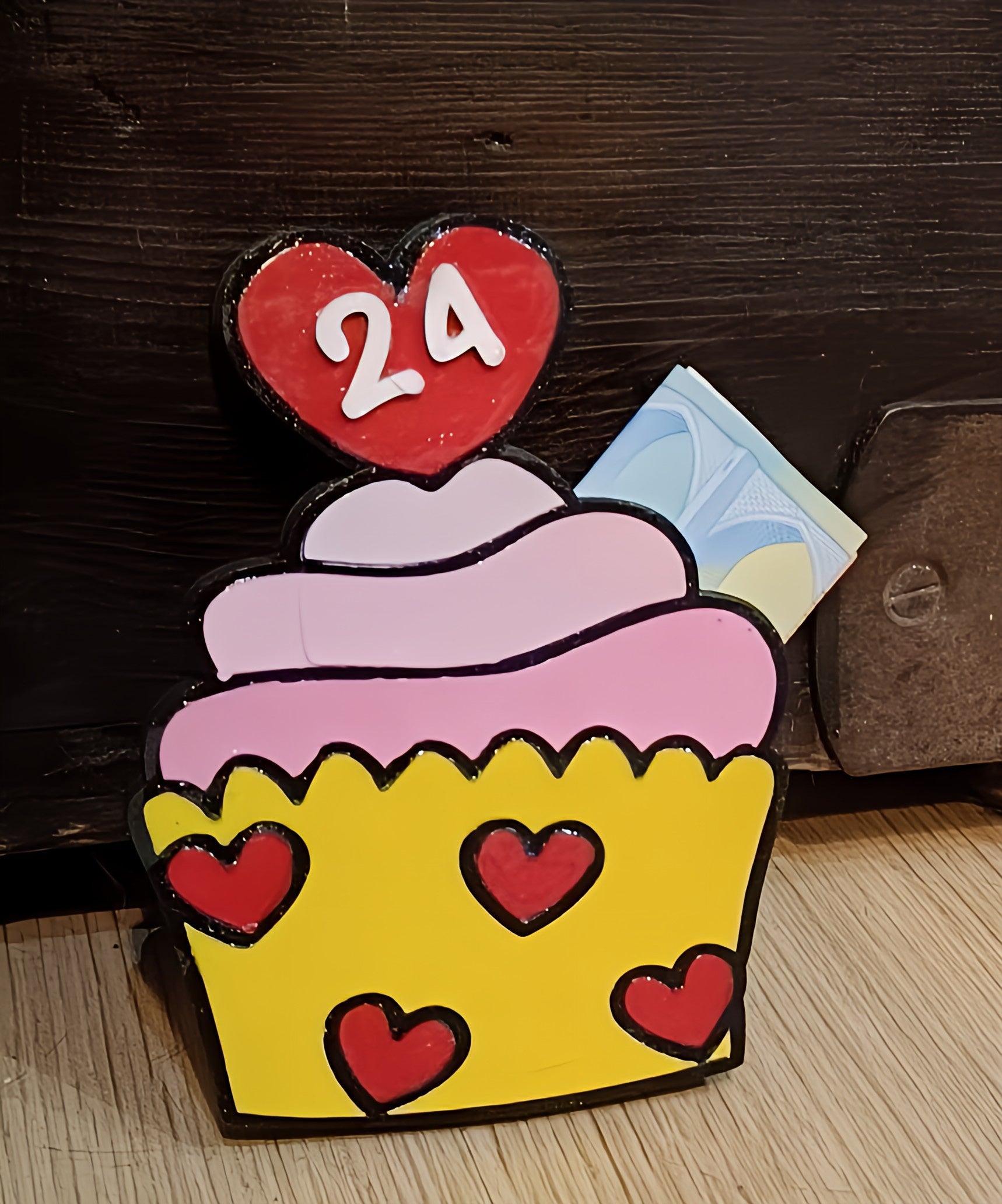 Cupcake-shaped calendar with heart decorations showing number 24 on a wooden surface