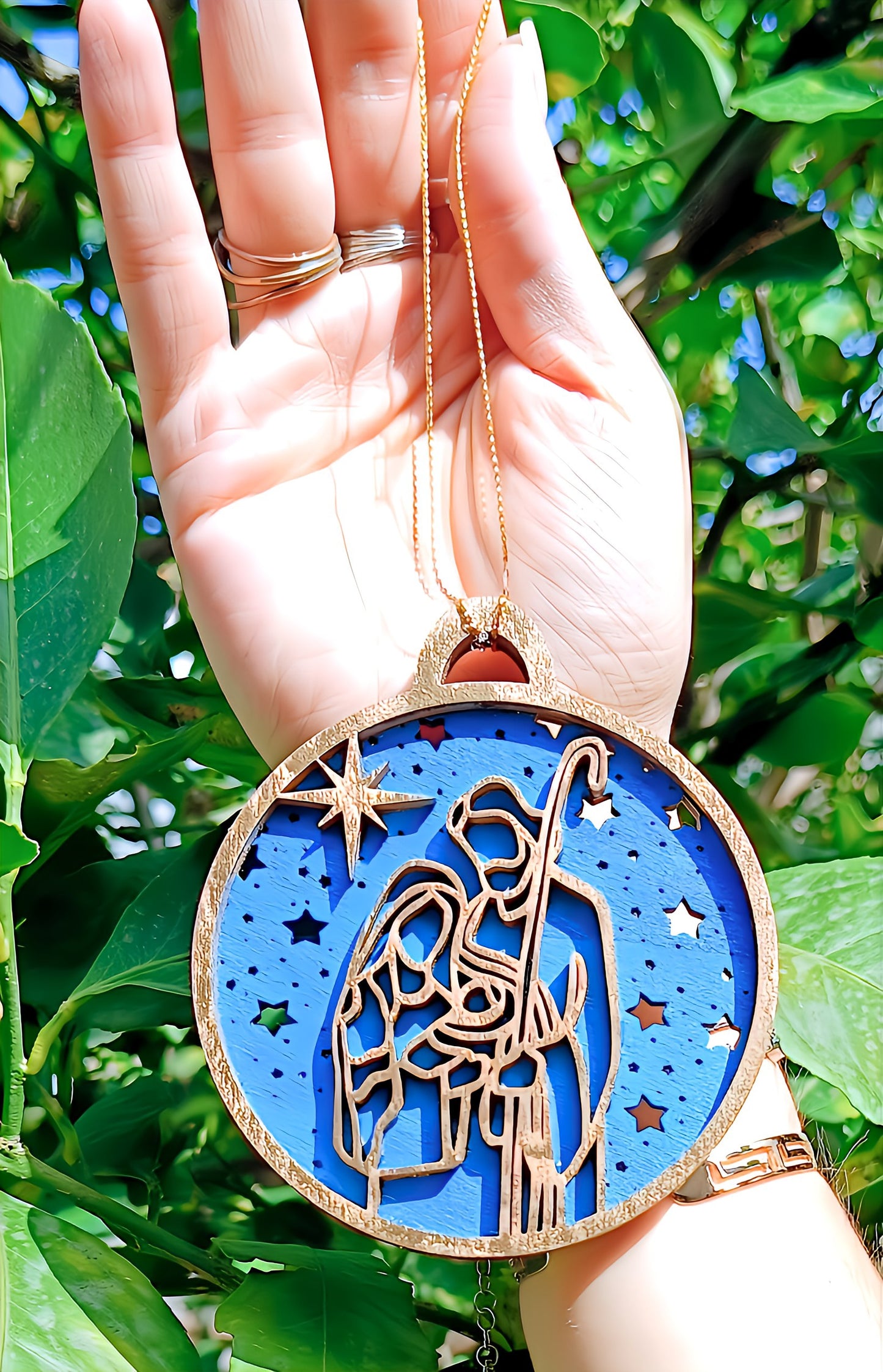 Hand holding a nativity Christmas ornament with blue star background outdoors