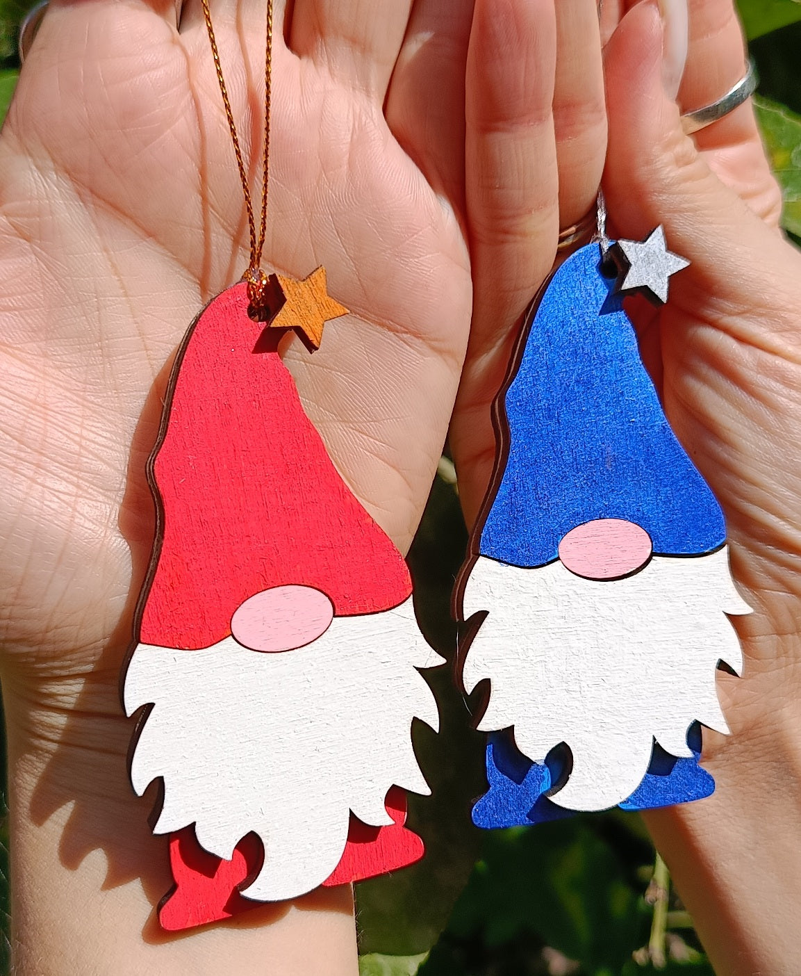Hand holding red and blue wooden gnome Christmas ornaments with star hats