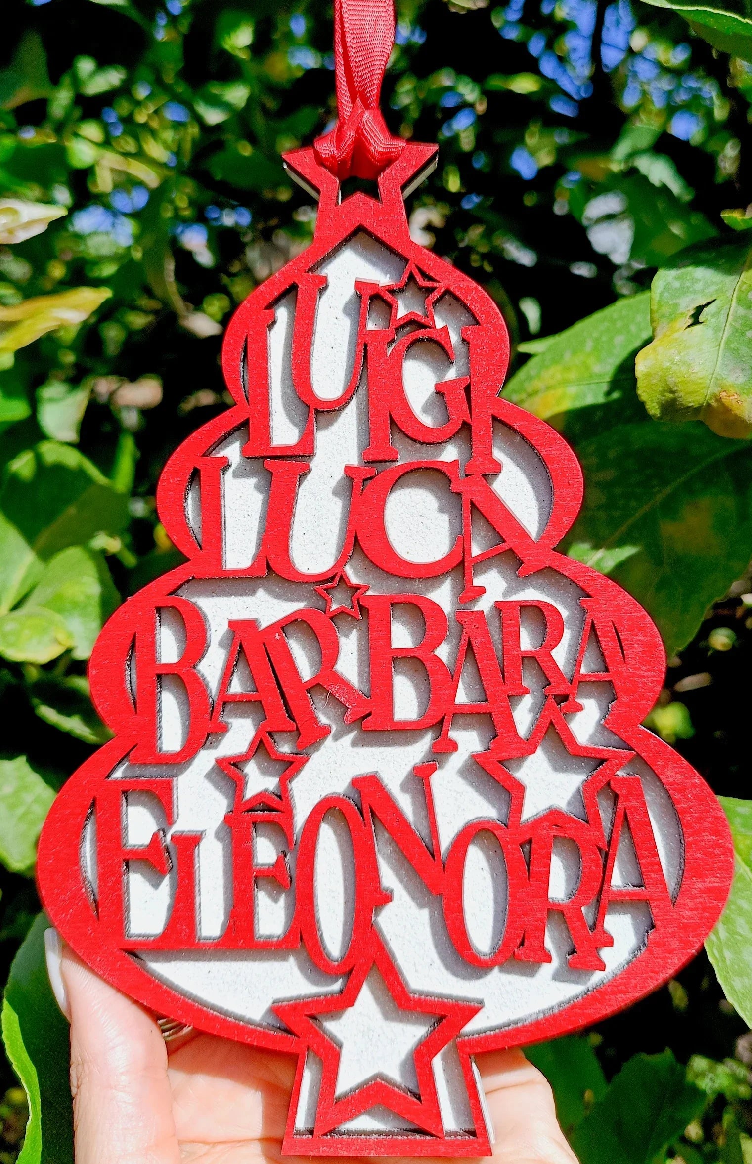 Red personalized Christmas tree ornament with names Lucia, Luca, Barbara, Eleonora outdoors