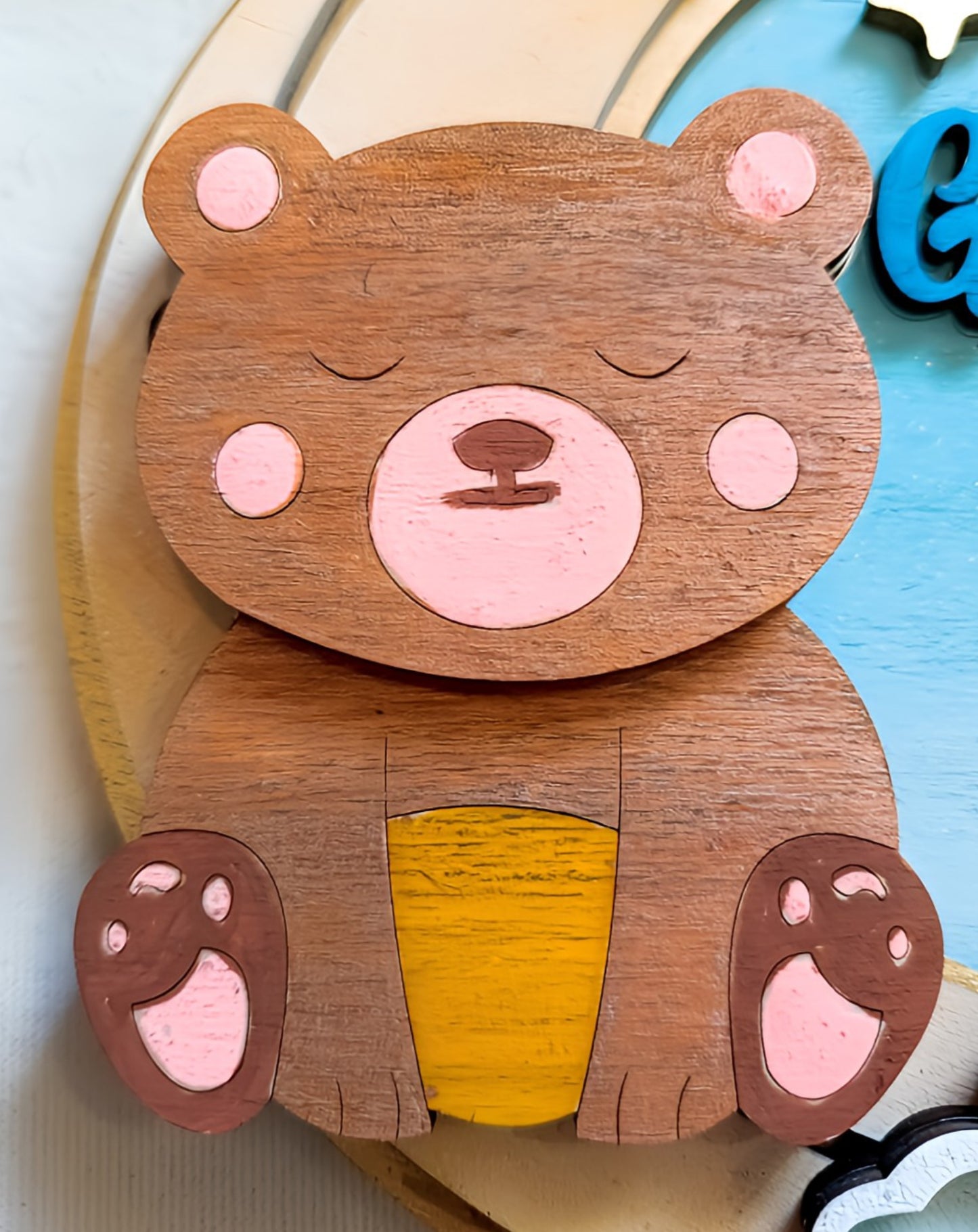 Wooden sleeping bear wall art with pink accents and yellow belly on a pastel background