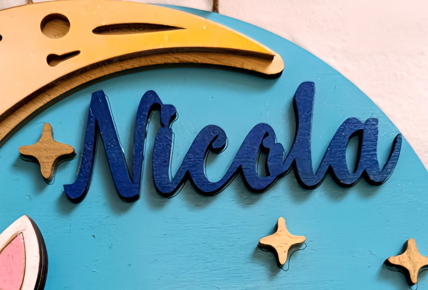 Wooden name sign Nicola with crescent moon and stars on blue background