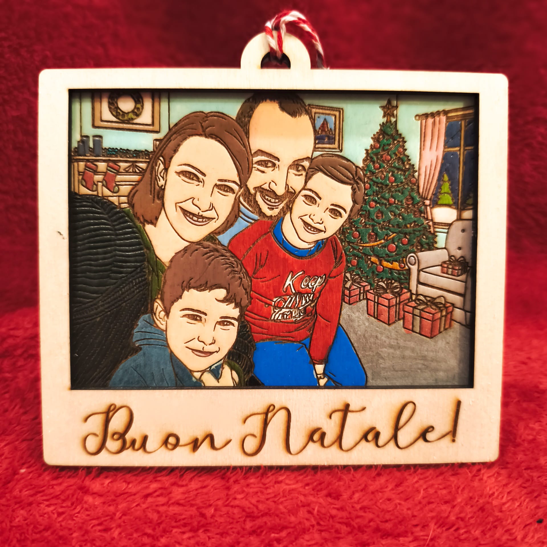 Ornamento natalizio in legno inciso con famiglia cartoon davanti all’albero di Natale e scritta “Buon Natale!”
