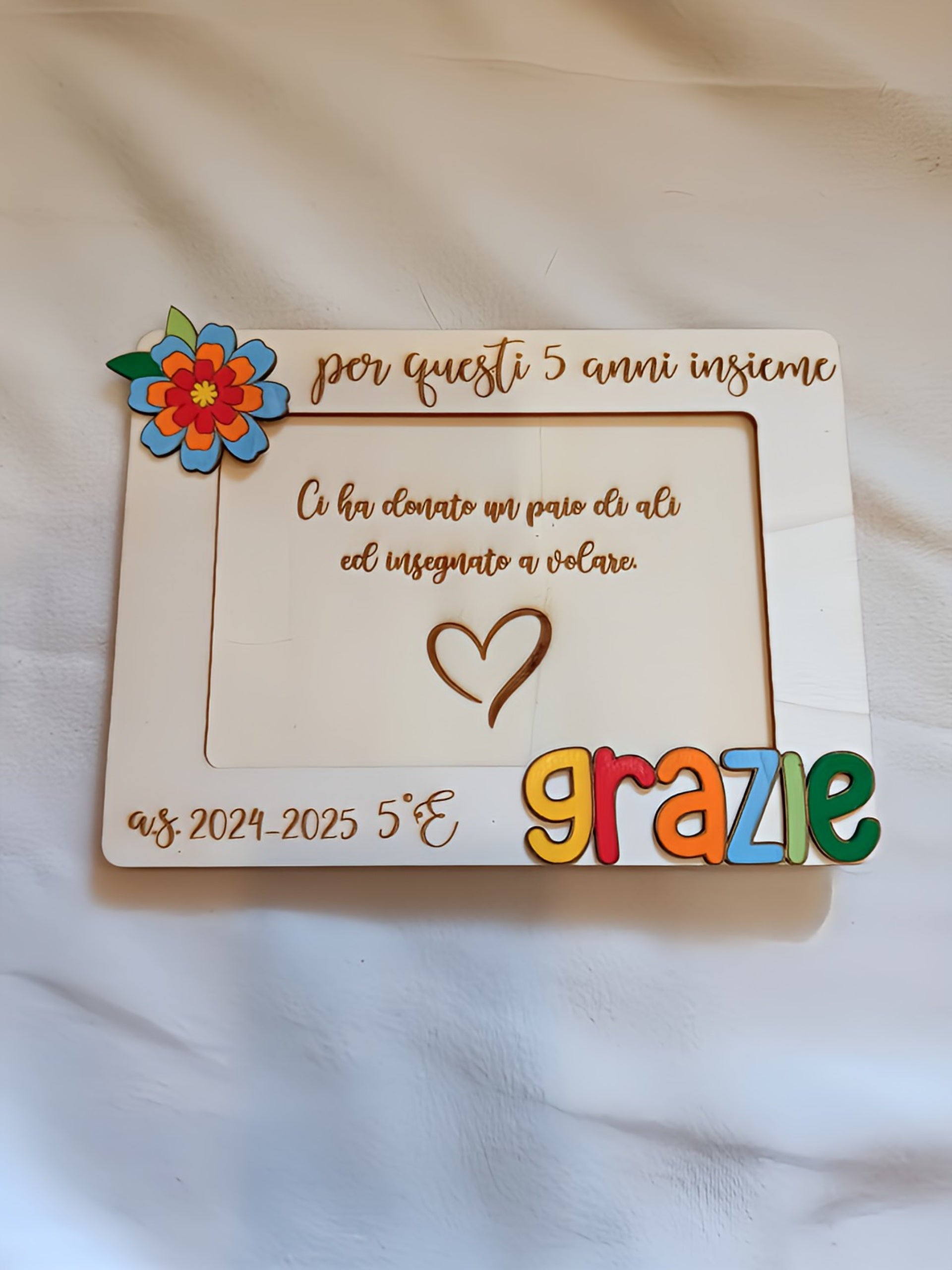 Portafoto rettangolare in legno bianco per maestra, con testo inciso a pirografia "per questi 5 anni insieme" e "Ci ha donato un paio di ali ed insegnato a volare", scritta tridimensionale "grazie" in lettere colorate giallo rosso arancio azzurro e verde, fiore decorativo multistrato in legno dipinto nell'angolo superiore sinistro, personalizzazione a.s. 2024-2025 5°E. Regalo fatto a mano per insegnante di fine anno scolastico.
