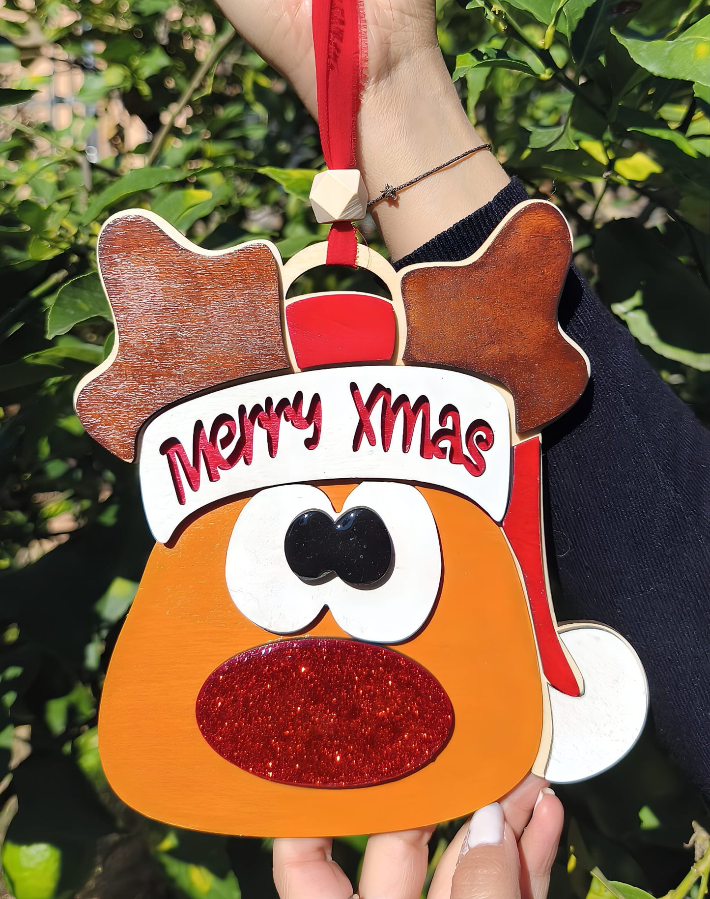 Hand holding reindeer Merry Xmas ornament with red glitter nose outdoors, Christmas decoration