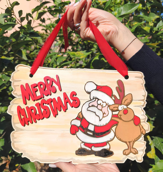 Hand holding wooden Merry Christmas sign with cartoon Santa and reindeer in garden