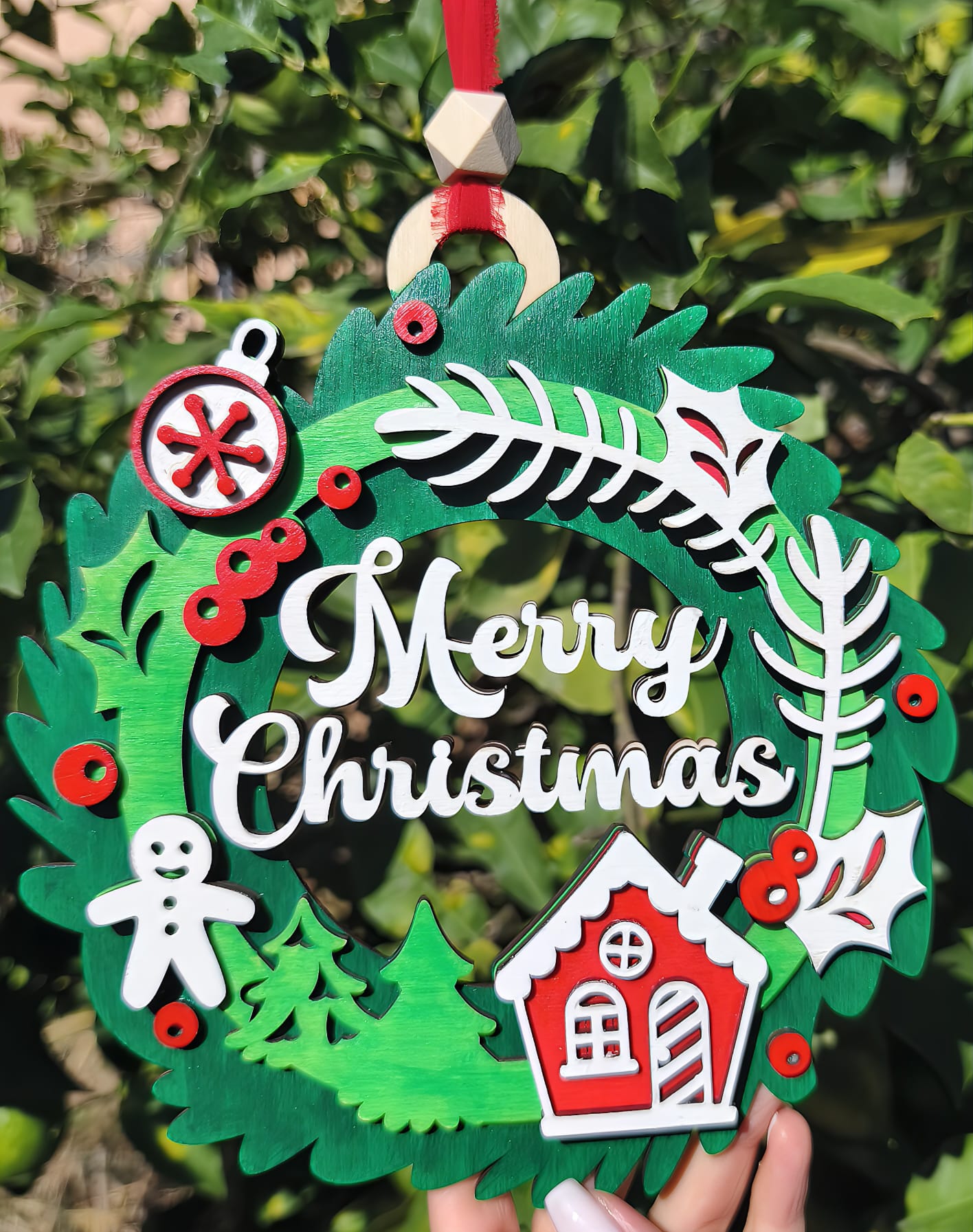 Wooden Merry Christmas wreath ornament with gingerbread man and red house, outdoors