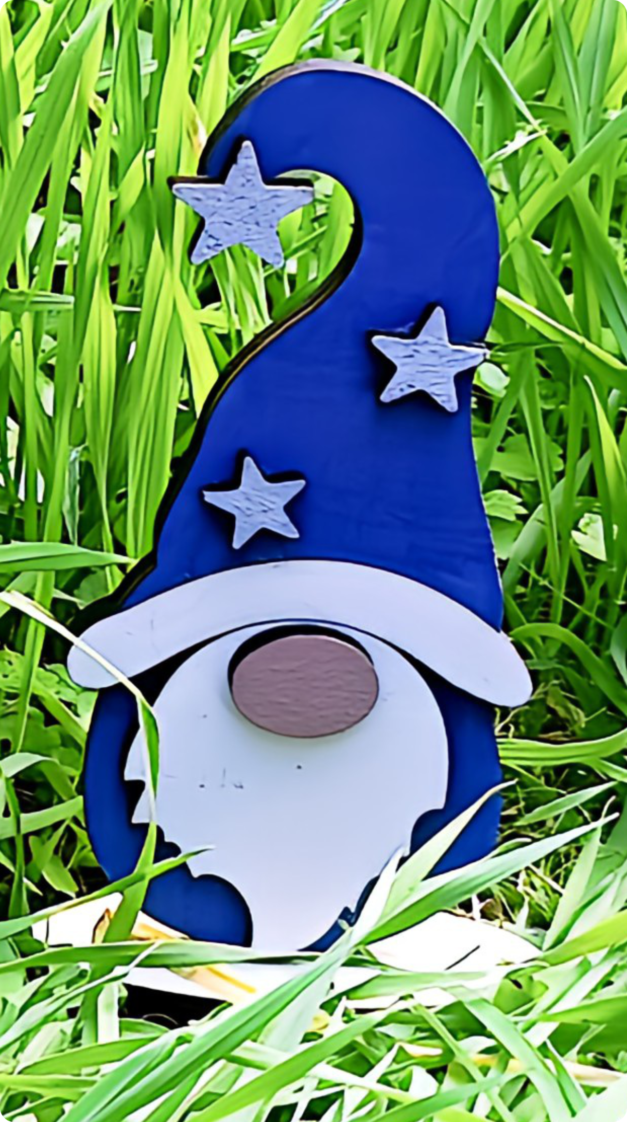 Wooden gnome with blue hat and stars in tall green grass garden decor