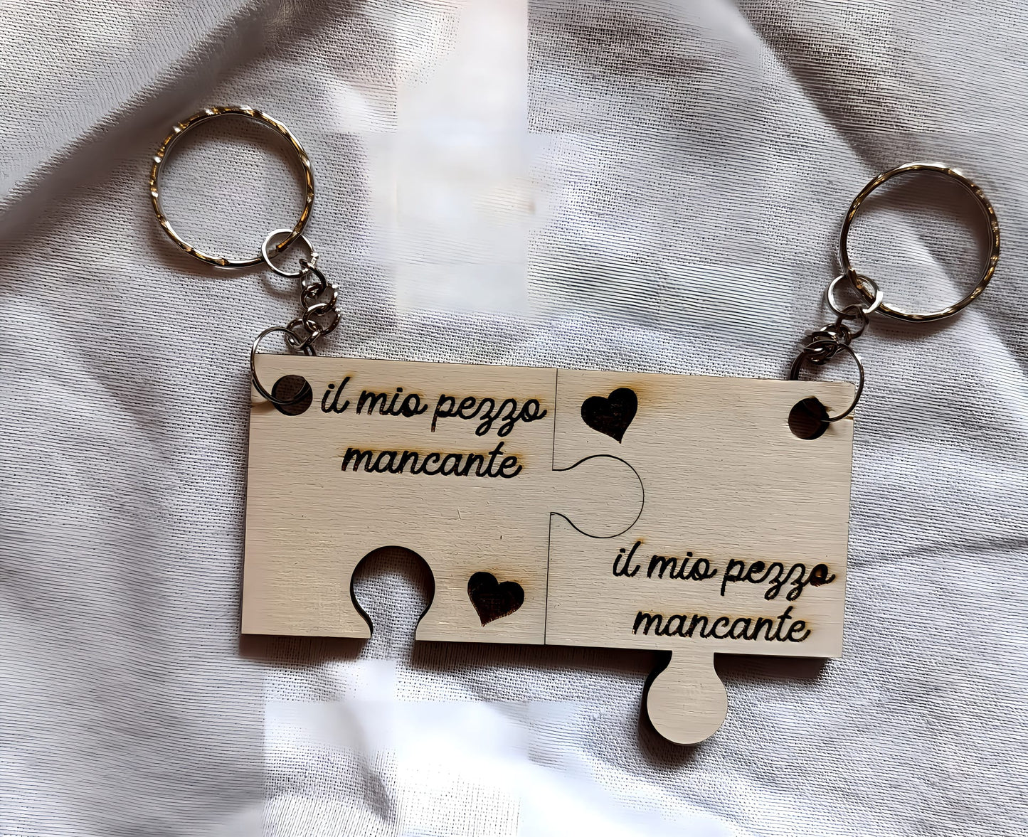 Wooden puzzle piece keychains with 'il mio pezzo mancante' engraved, heart cutouts, on fabric