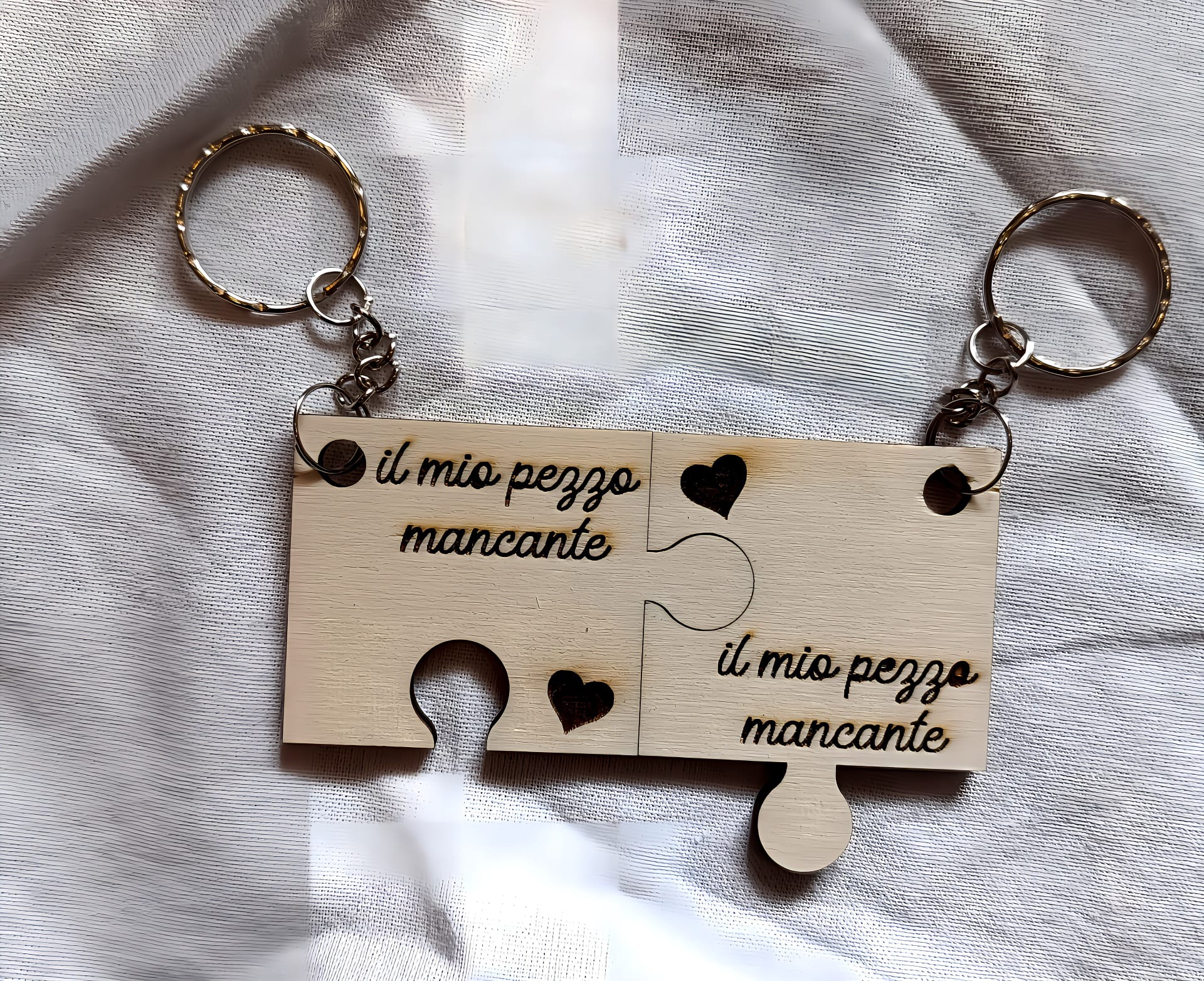 Wooden puzzle piece keychains with 'il mio pezzo mancante' engraved, heart cutouts, on fabric
