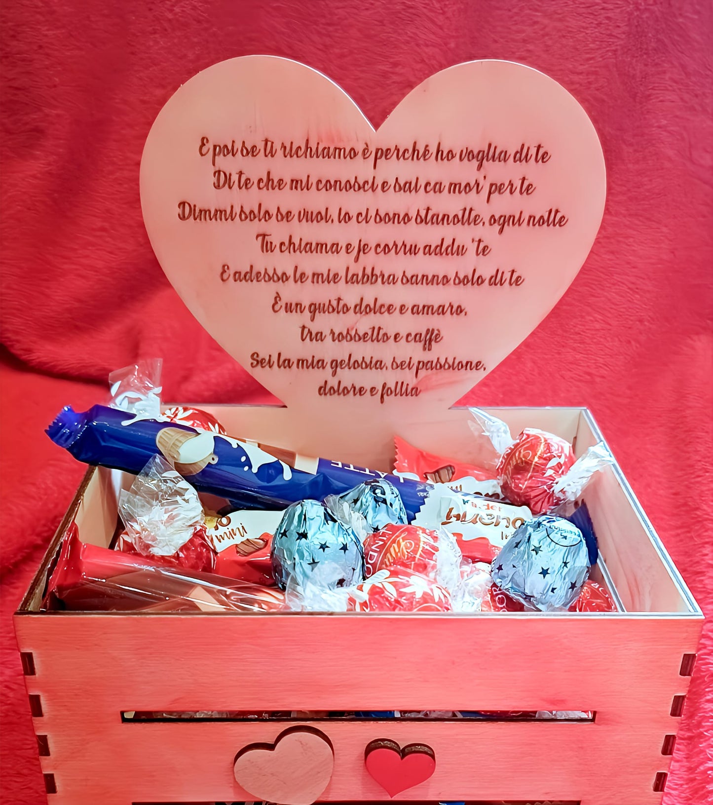 Wooden gift box with assorted chocolates and a heart-shaped plaque with Italian love poem, on red background