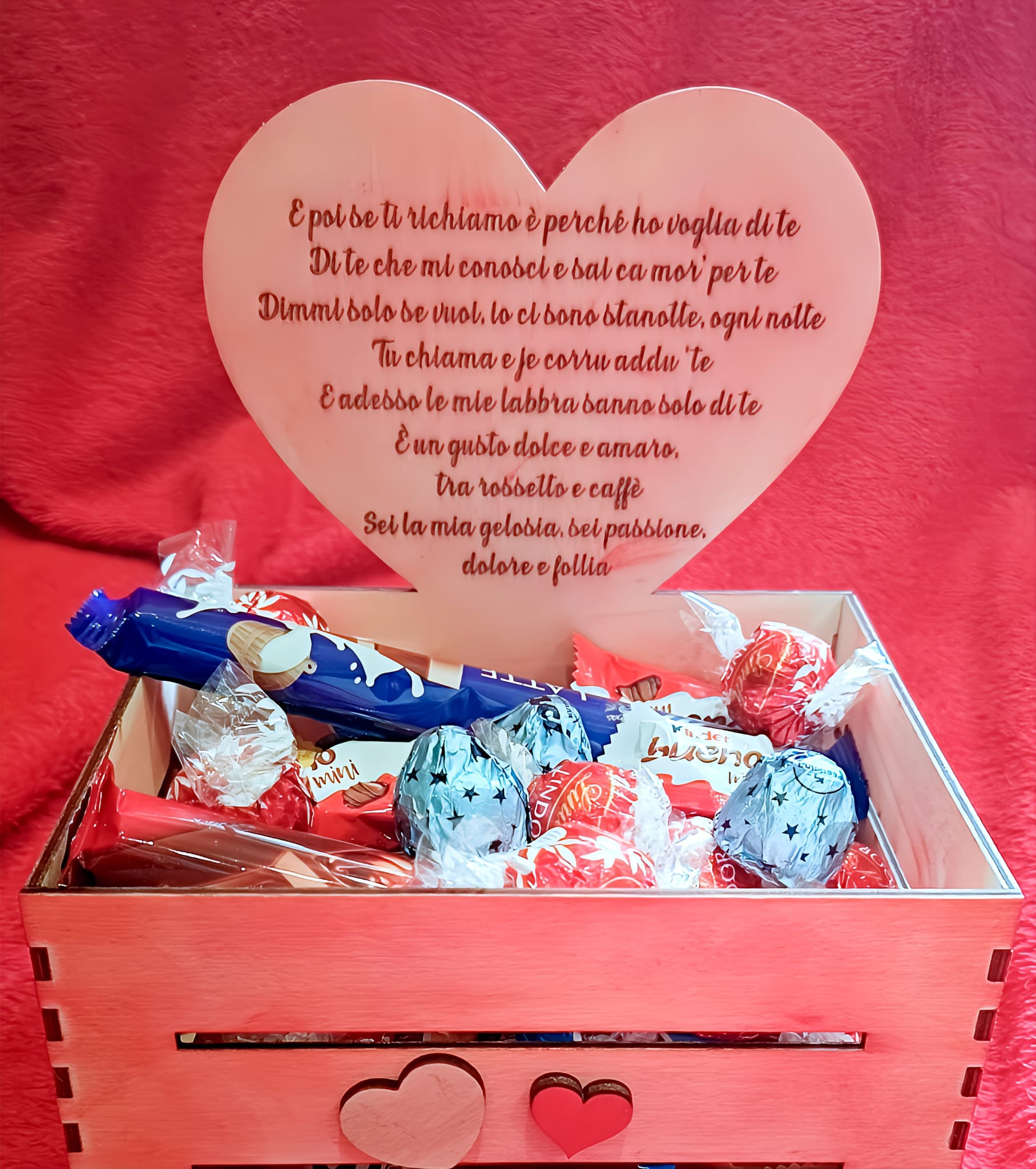 Wooden gift box with assorted chocolates and a heart-shaped plaque with Italian love poem, on red background