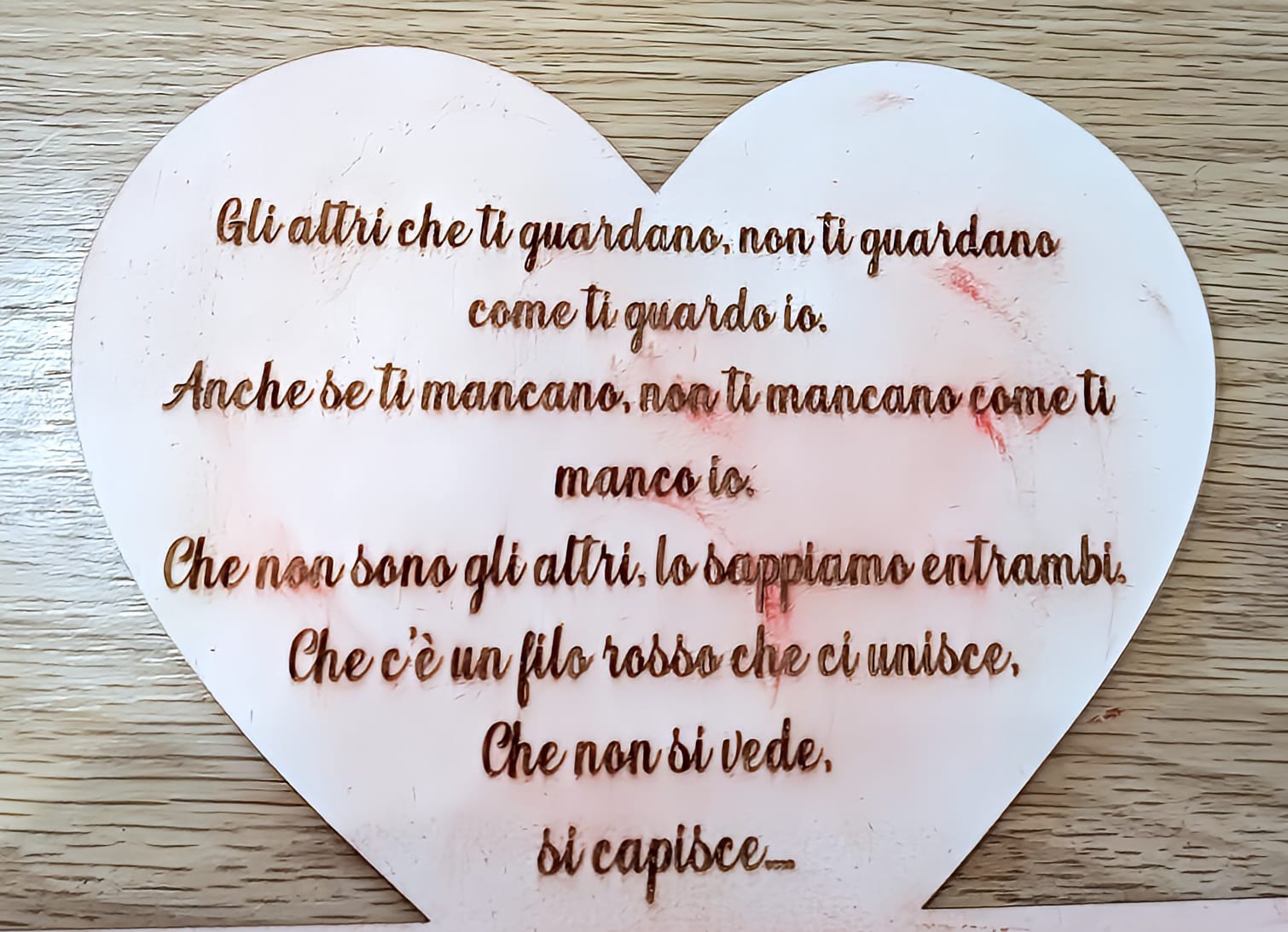 Heart-shaped plaque with Italian engraved love message on light wood background
